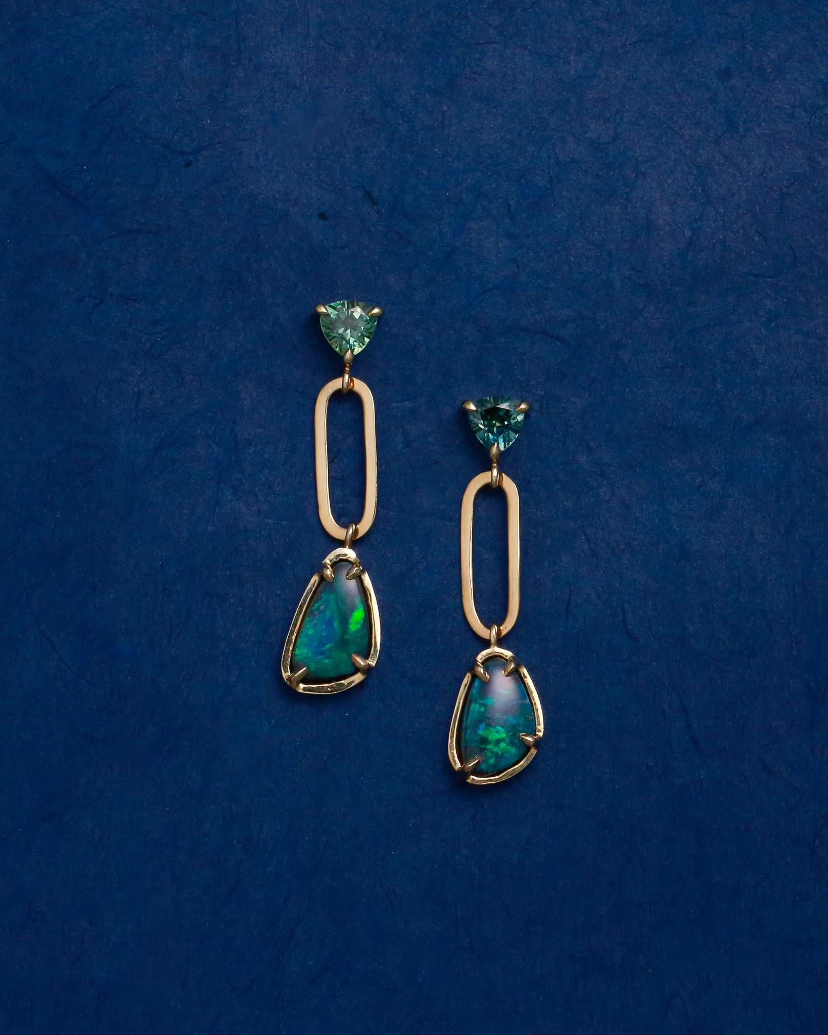 Pair of gold drop earrings with blue opals on a blue background