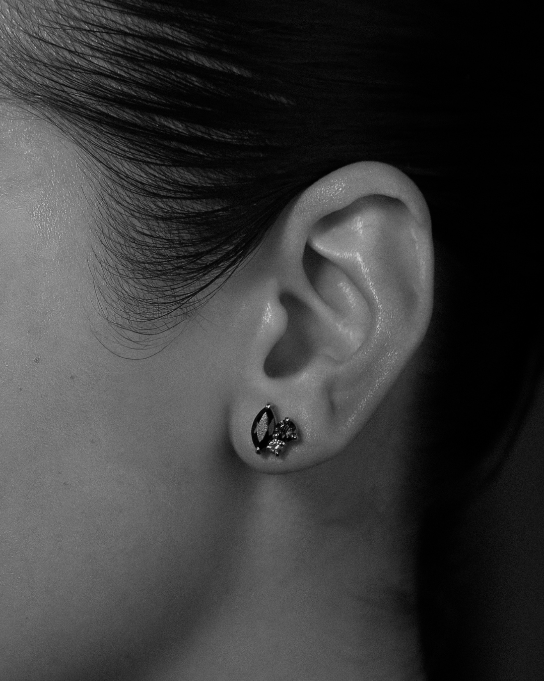Close-up of an ear with a gemstone stud earring on a dark background