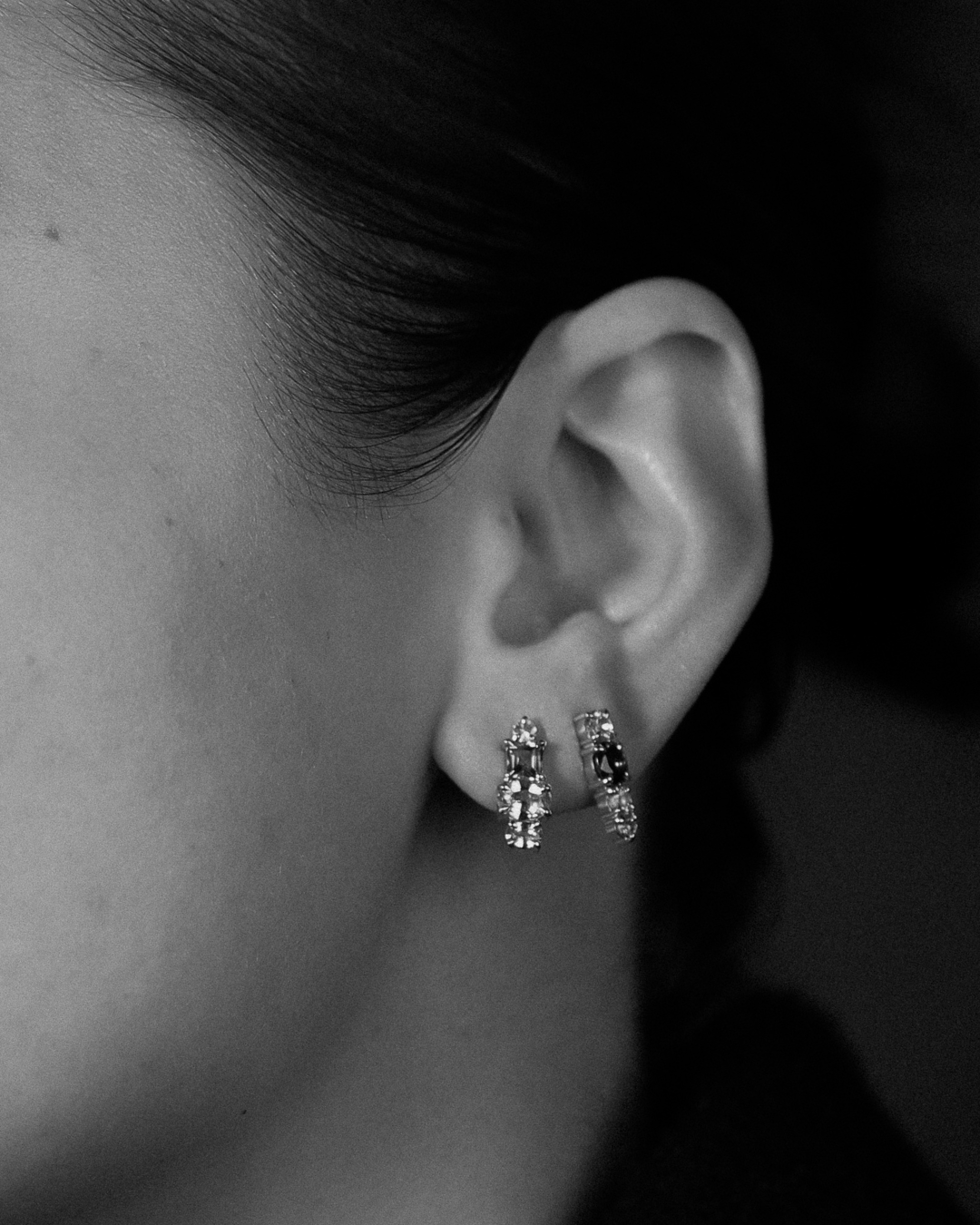 Close-up of an ear wearing two gemstone stud drop earrings with a dark background