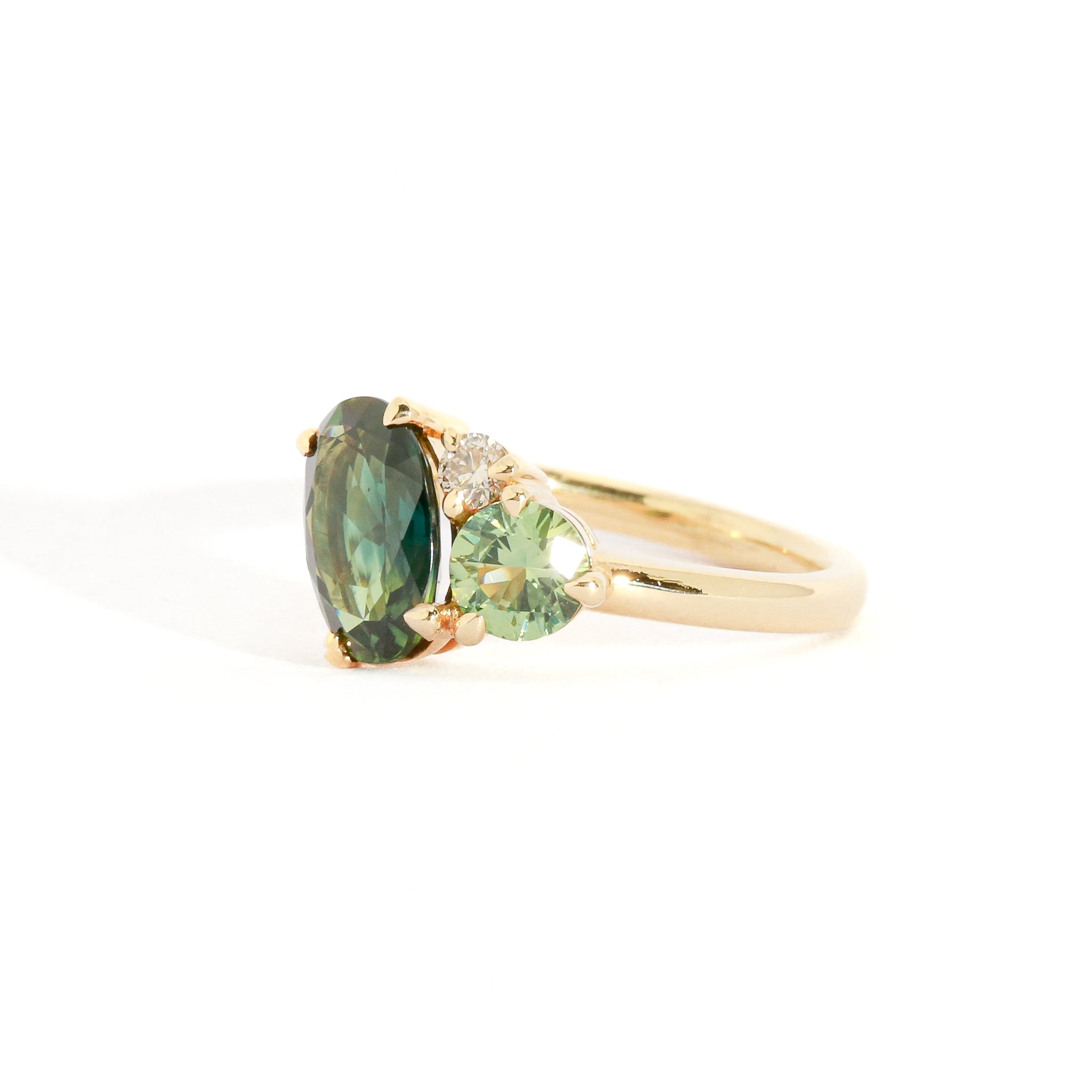 Asymmetrical gold three stone ring with a central oval cut green sapphire.
