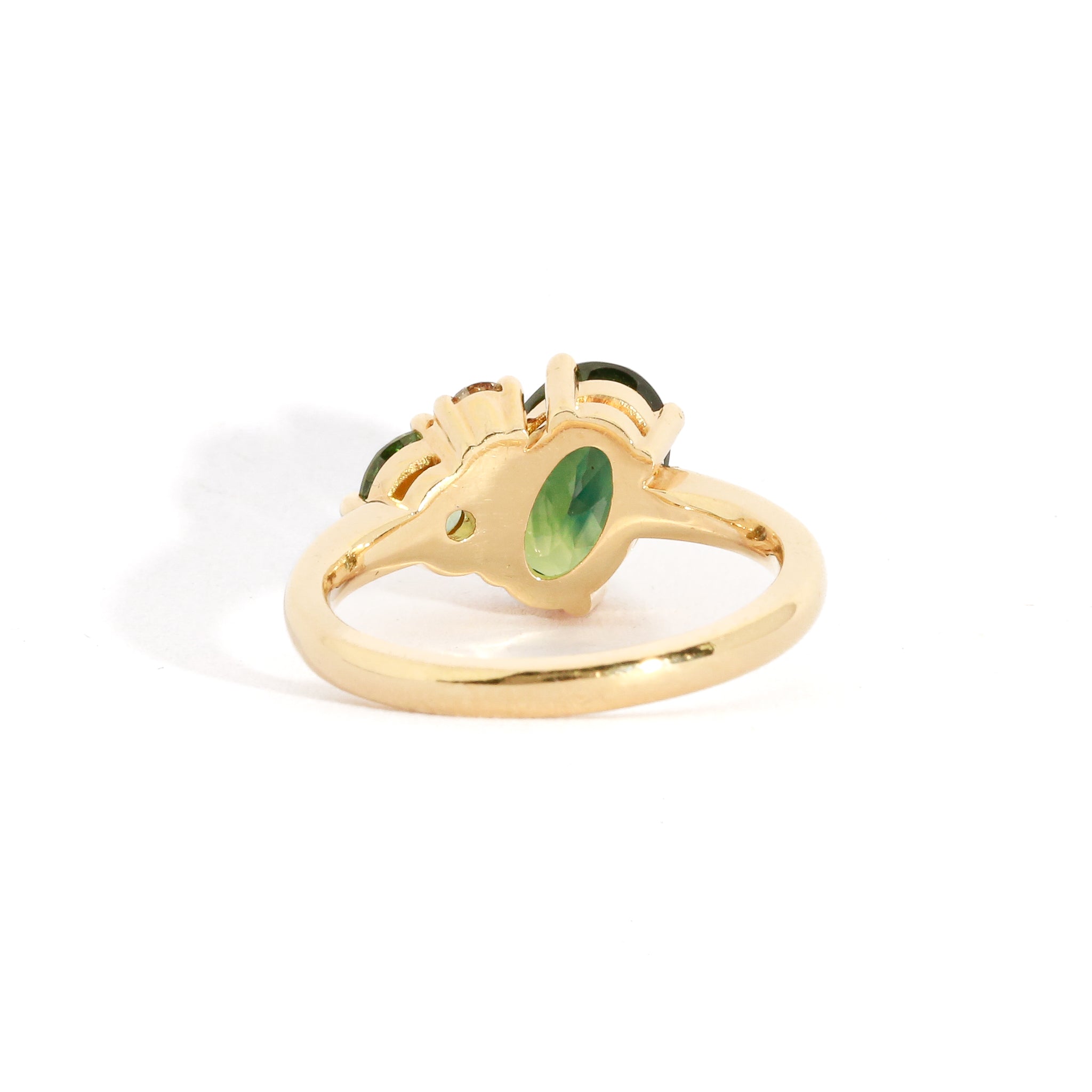 Asymmetrical gold three stone ring with a central oval cut green sapphire.