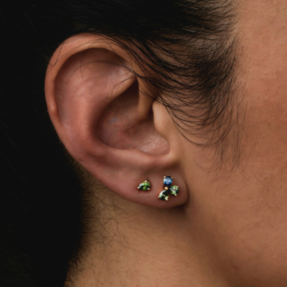 Close-up of a person's ear wearing small stud earrings of green pear cut sapphires.