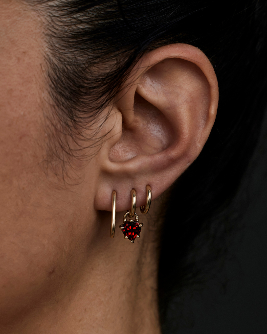 Gold huggie earrings with red heart-shaped garnet on an ear stack