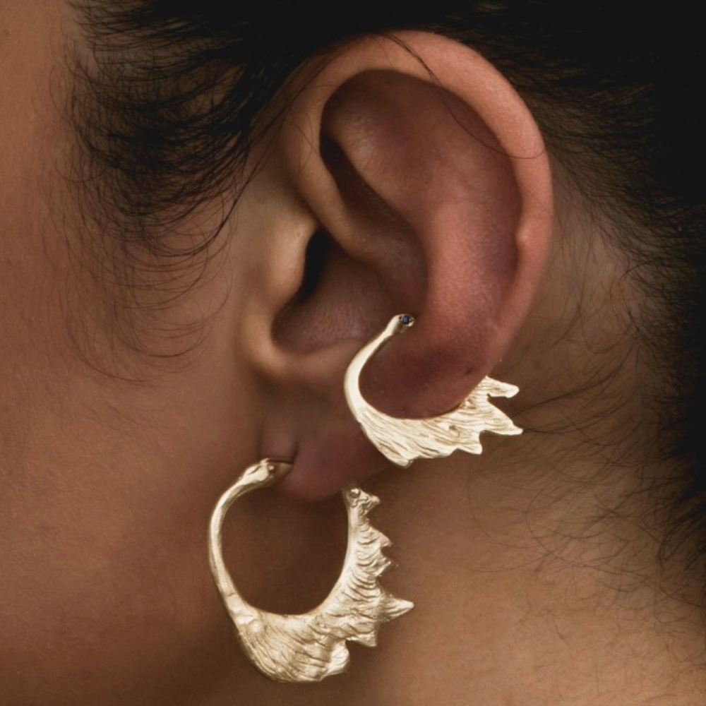 Lifestyle close-up of the sculptural yellow gold serpent earrings worn on the ear with colourful gemstone accents.