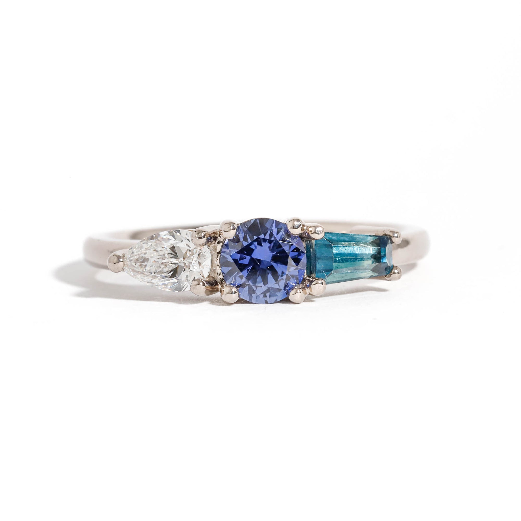 Three Stone Ring with Centre Blue Sapphire, Round White Diamond and Tapered Blue Baguette Sapphire Side Stones in 18 Carat White Gold