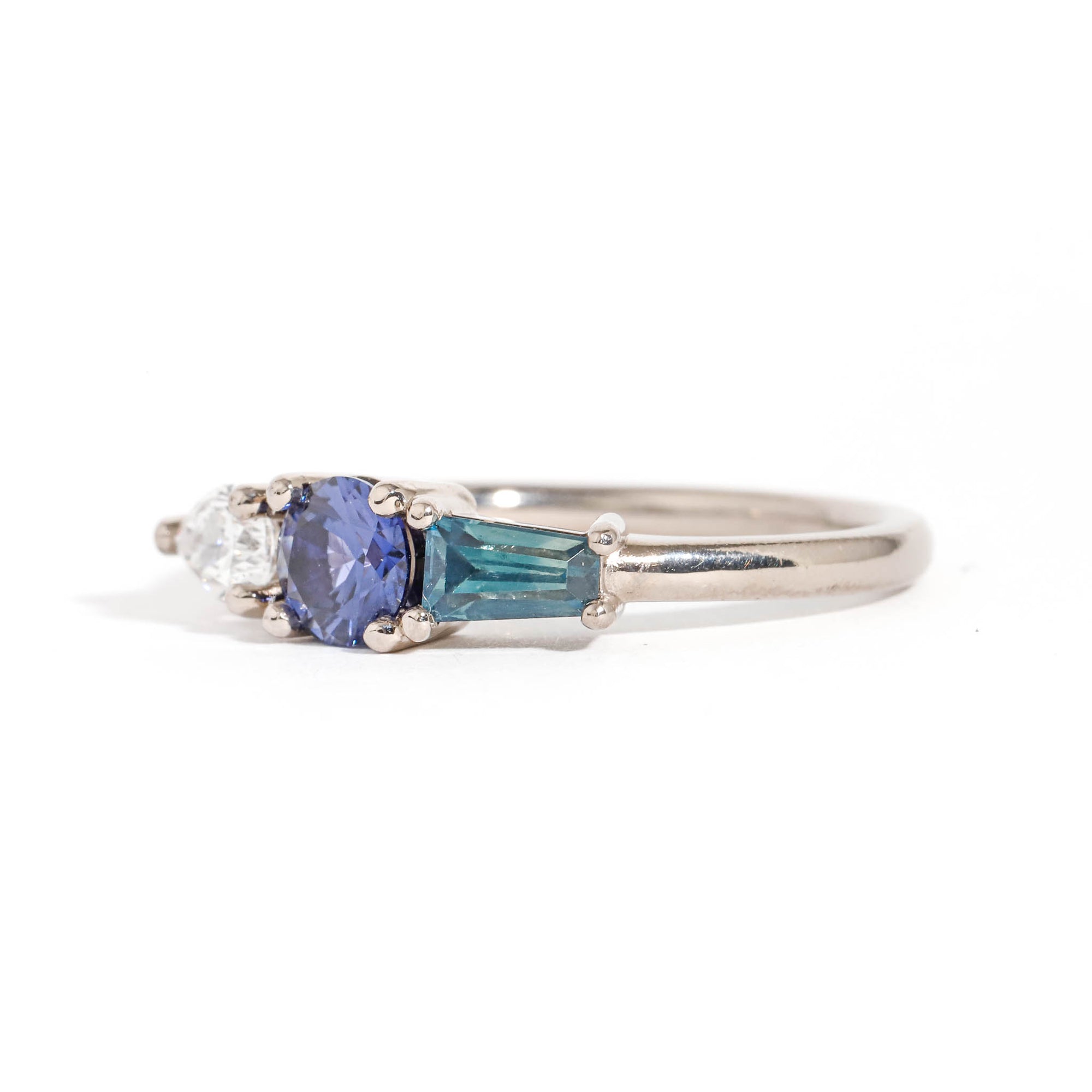 Three Stone Ring with Centre Blue Sapphire, Round White Diamond and Tapered Blue Baguette Sapphire Side Stones in 18 Carat White Gold