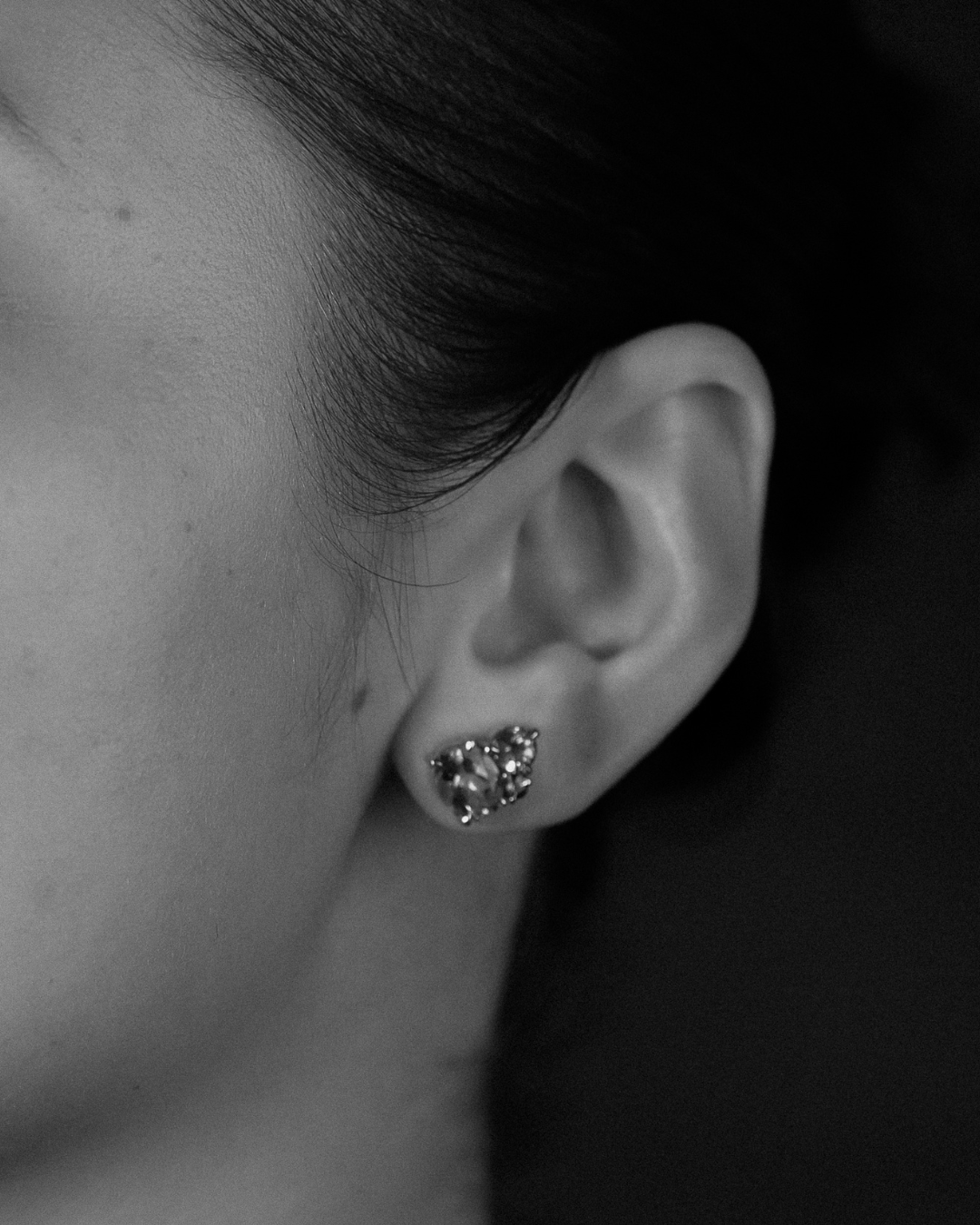 Close-up of an ear wearing a gemstone stud earring with a dark background