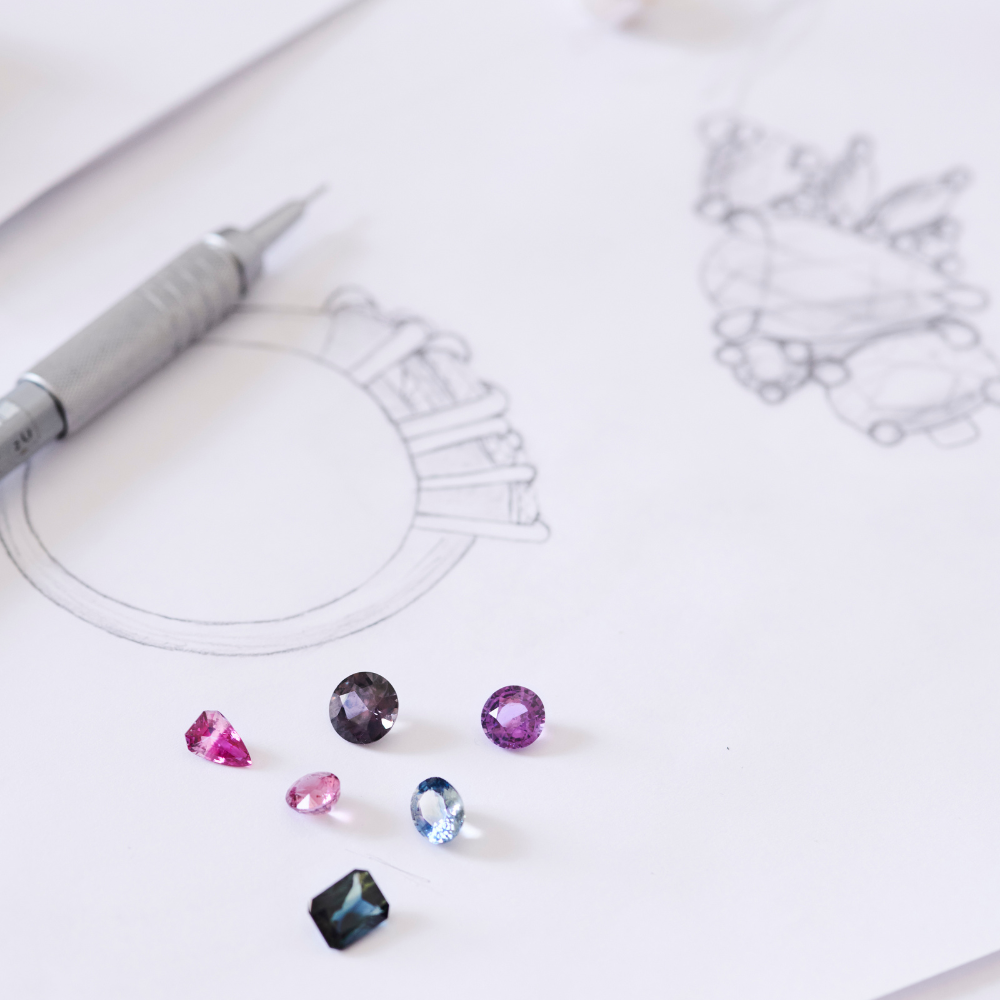 Colorful gemstones on a white surface with a pen and jewelry design.