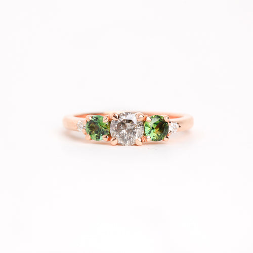  Featured in 18 carat rose gold, a five stone ring with one central round salt and pepper diamond, two round ethically sourced green Australian sapphires, and two round white diamonds. 