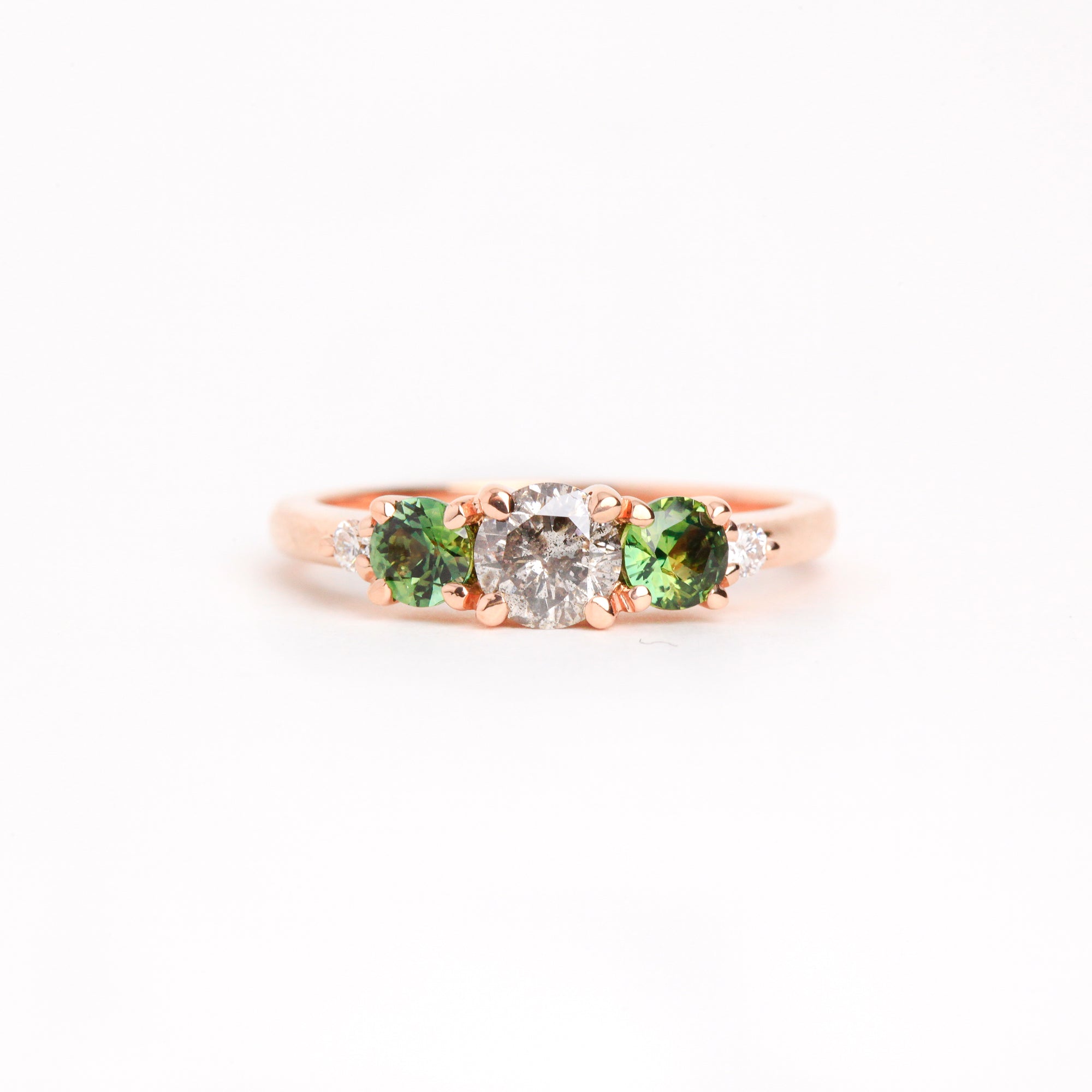  Featured in 18 carat rose gold, a five stone ring with one central round salt and pepper diamond, two round ethically sourced green Australian sapphires, and two round white diamonds. 