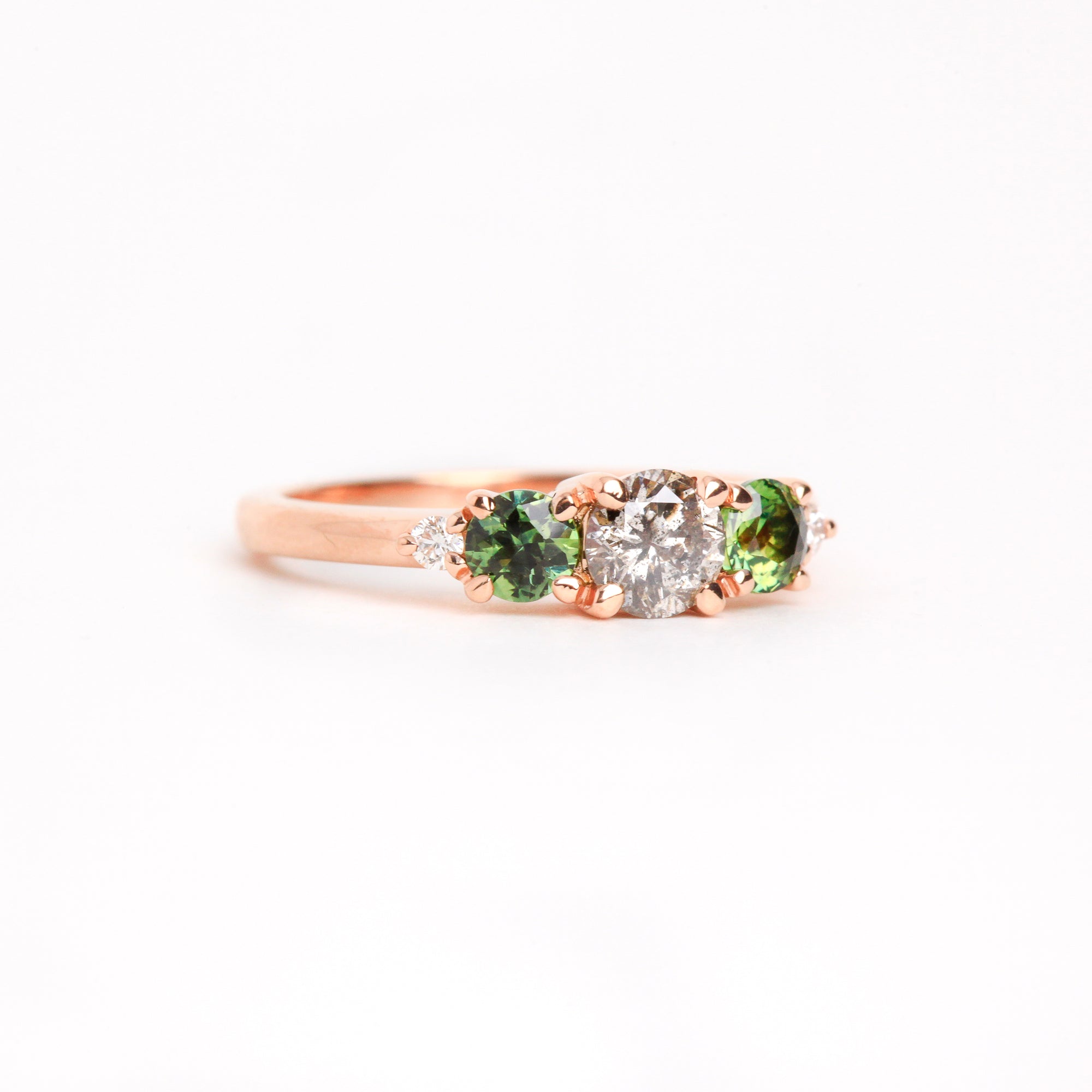  Featured in 18 carat rose gold, a five stone ring with one central round salt and pepper diamond, two round ethically sourced green Australian sapphires, and two round white diamonds. 